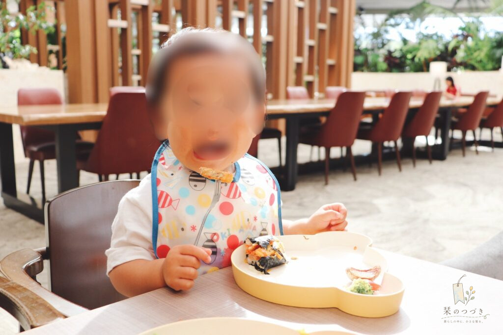 ベビーチェアに座り、スタイをつけてフォークでごはんを食べる次女